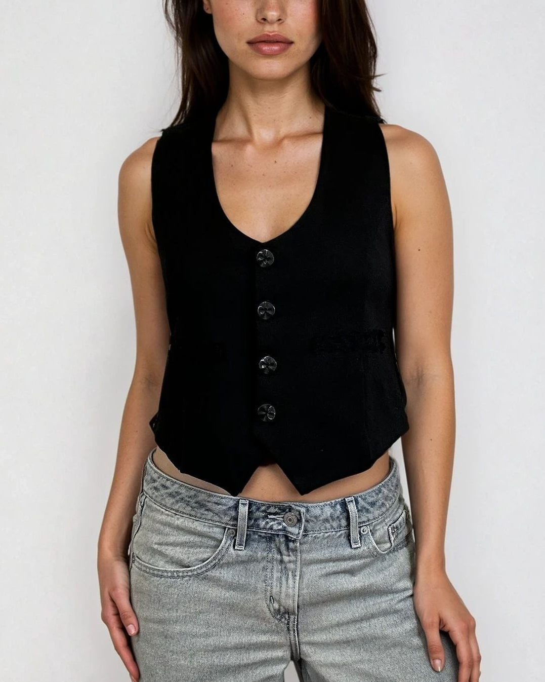 Woman wearing a black ponte vest top with buttons and crochet material on the side and gray jeans against a white background - Pete Collection