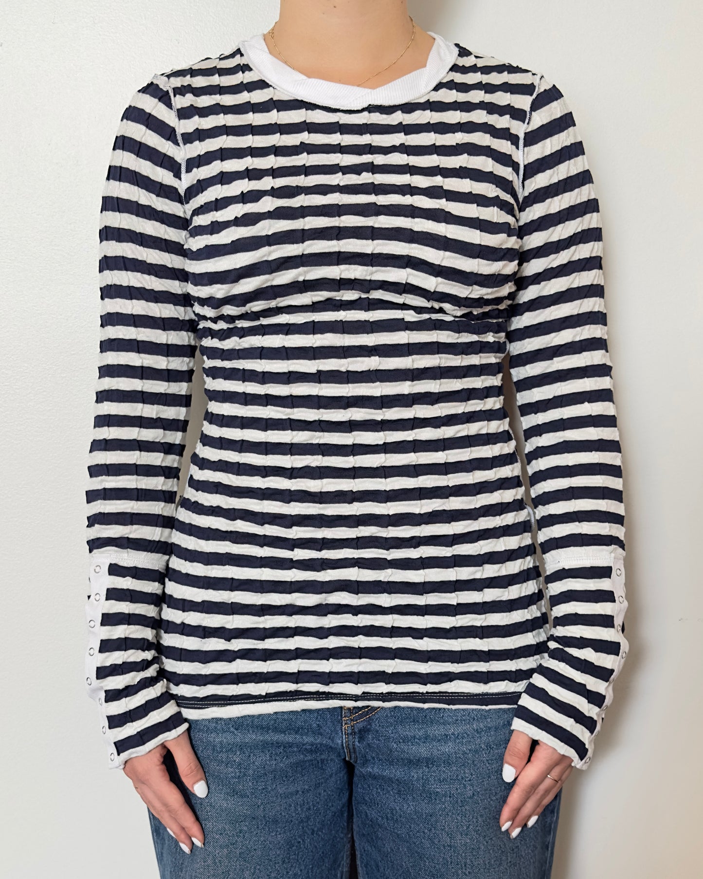 Female model wearing a scrunched striped long sleeve top in a navy and white color with a crew neck cut and buttons on the sleeves