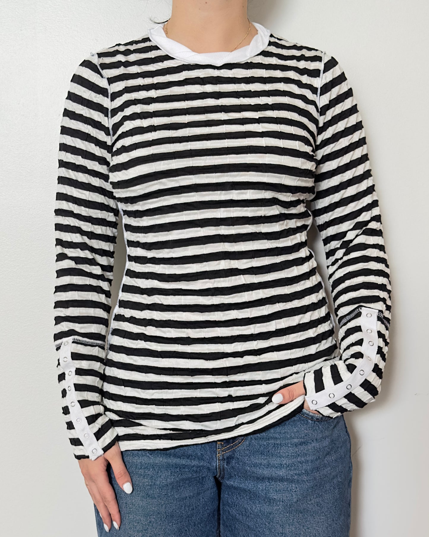 Female model wearing a scrunched striped long sleeve top in a black and white color with a crew neck cut and buttons on the sleeves