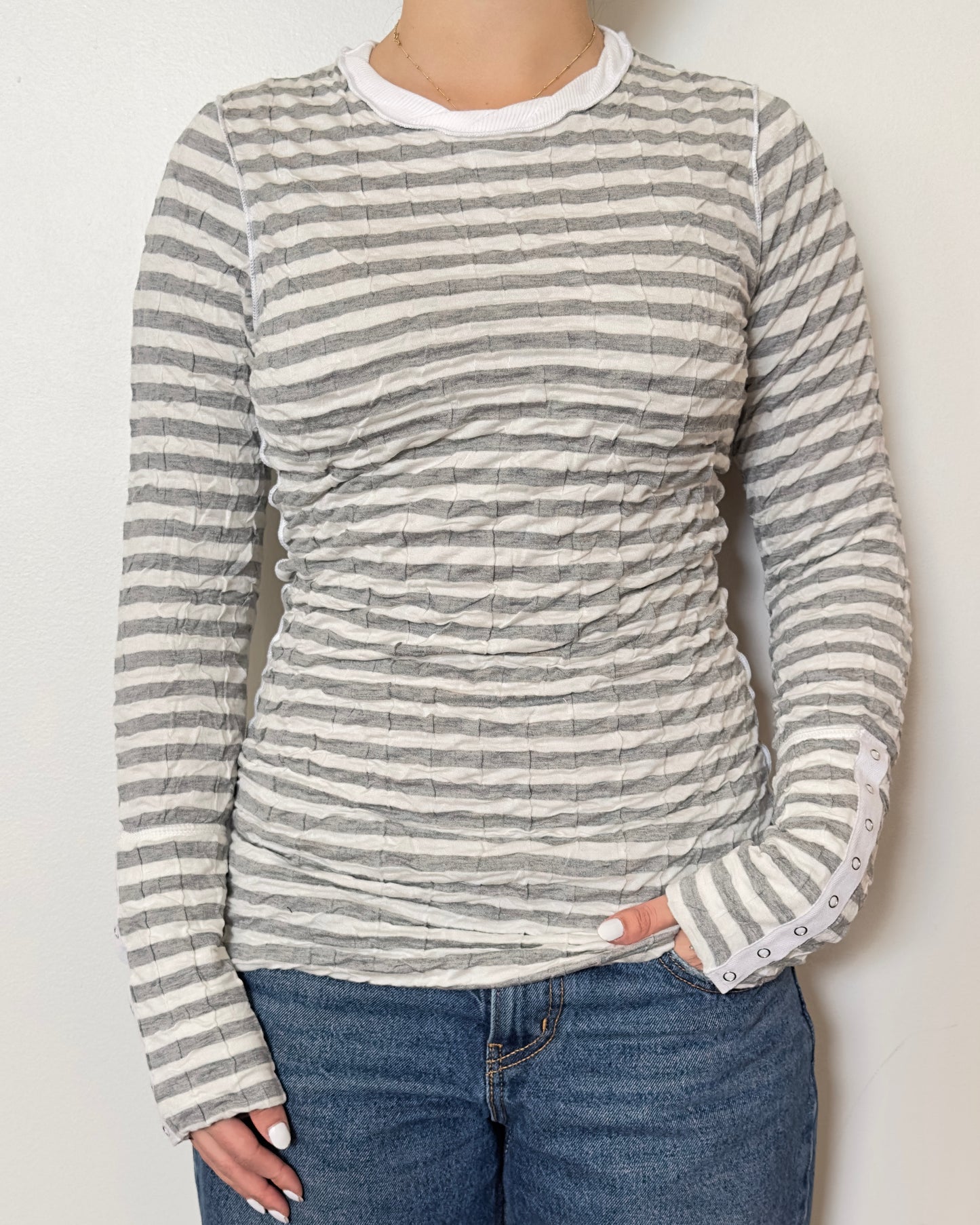 Female model wearing a scrunched striped long sleeve top in a grey and white color with a crew neck cut and buttons on the sleeves