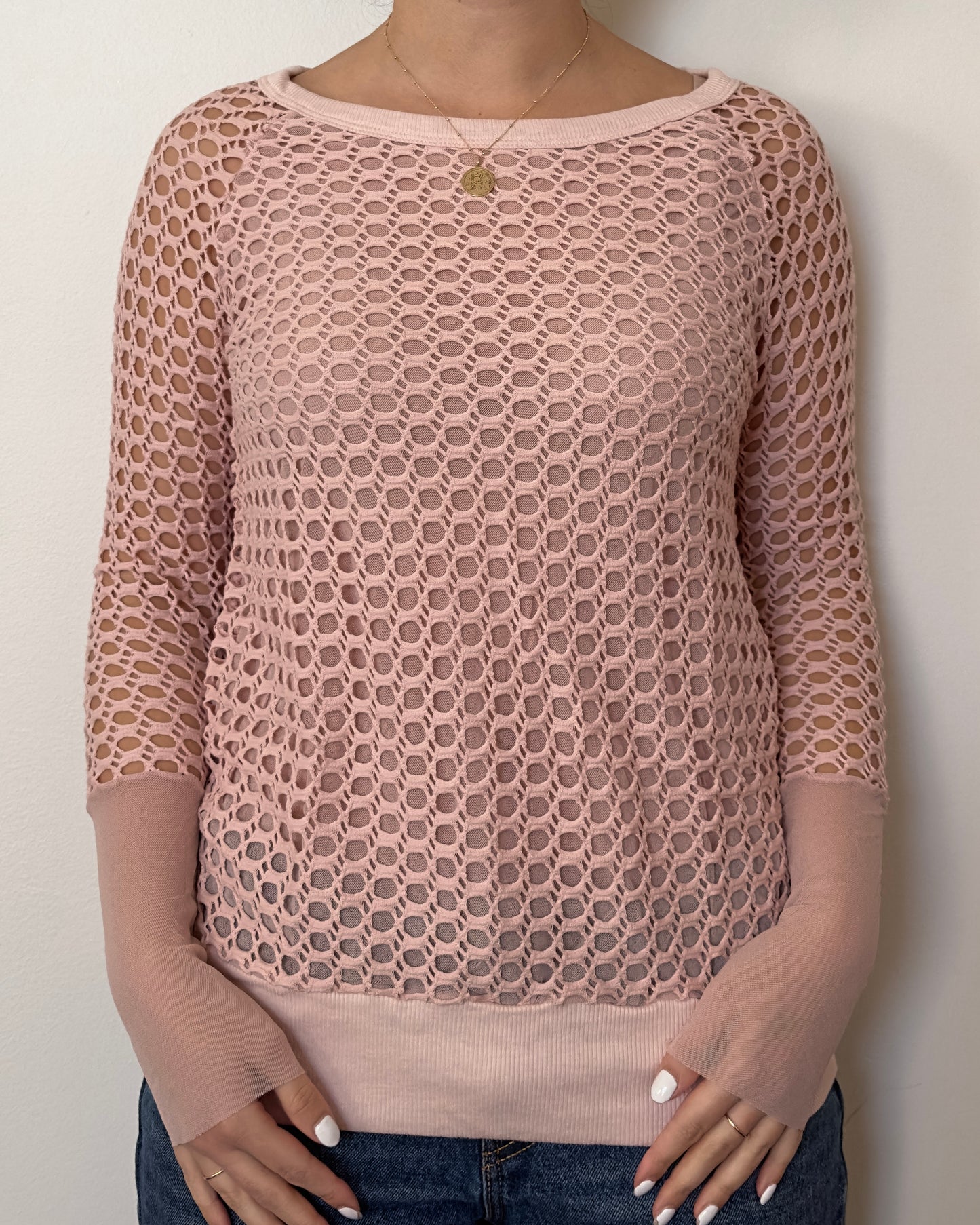 Female model wearing a crochet long sleeve top with part mesh sleeves in a blush pink color with a crew neck cut