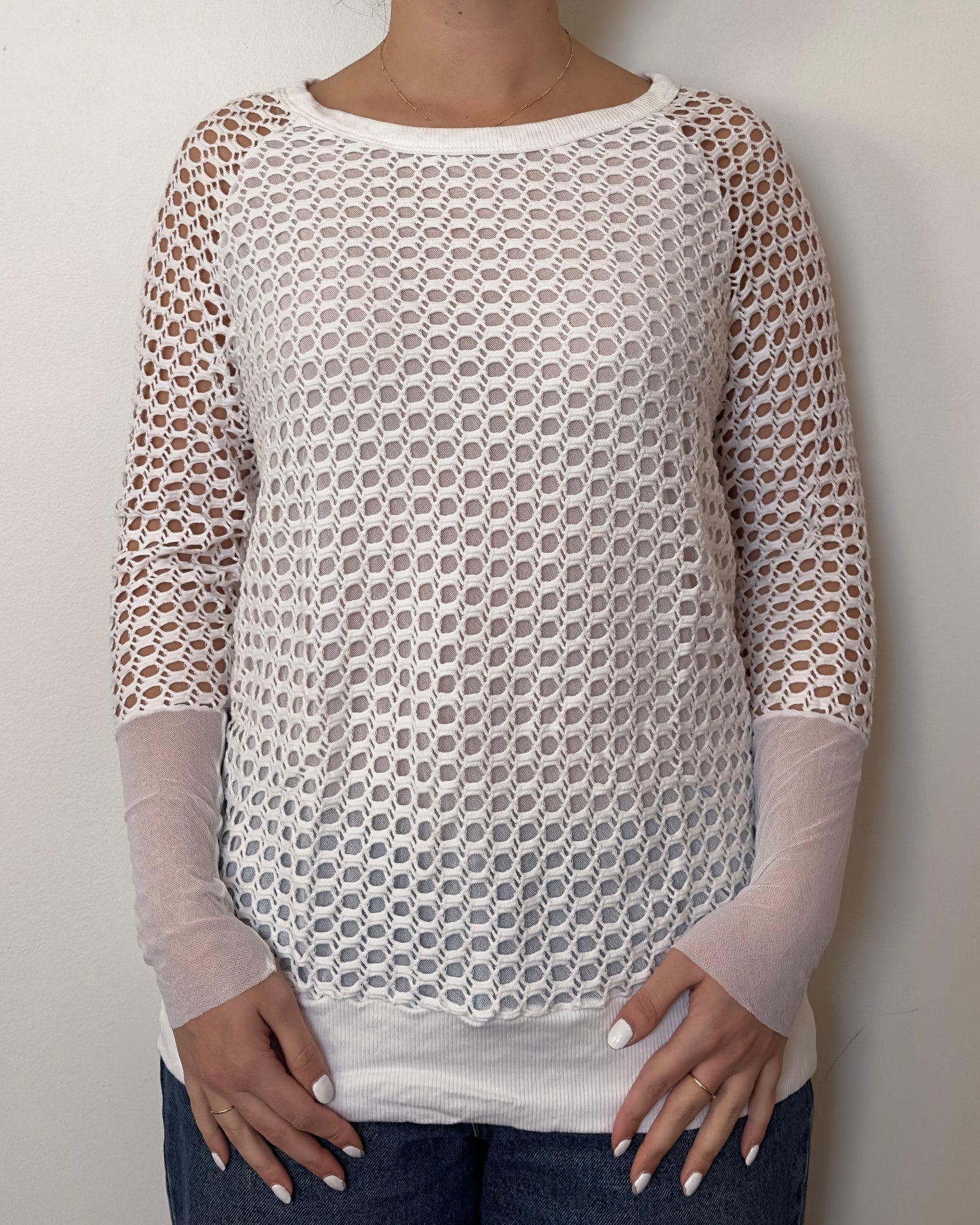 Female model wearing a crochet long sleeve top with part mesh sleeves in a white color with a crew neck cut