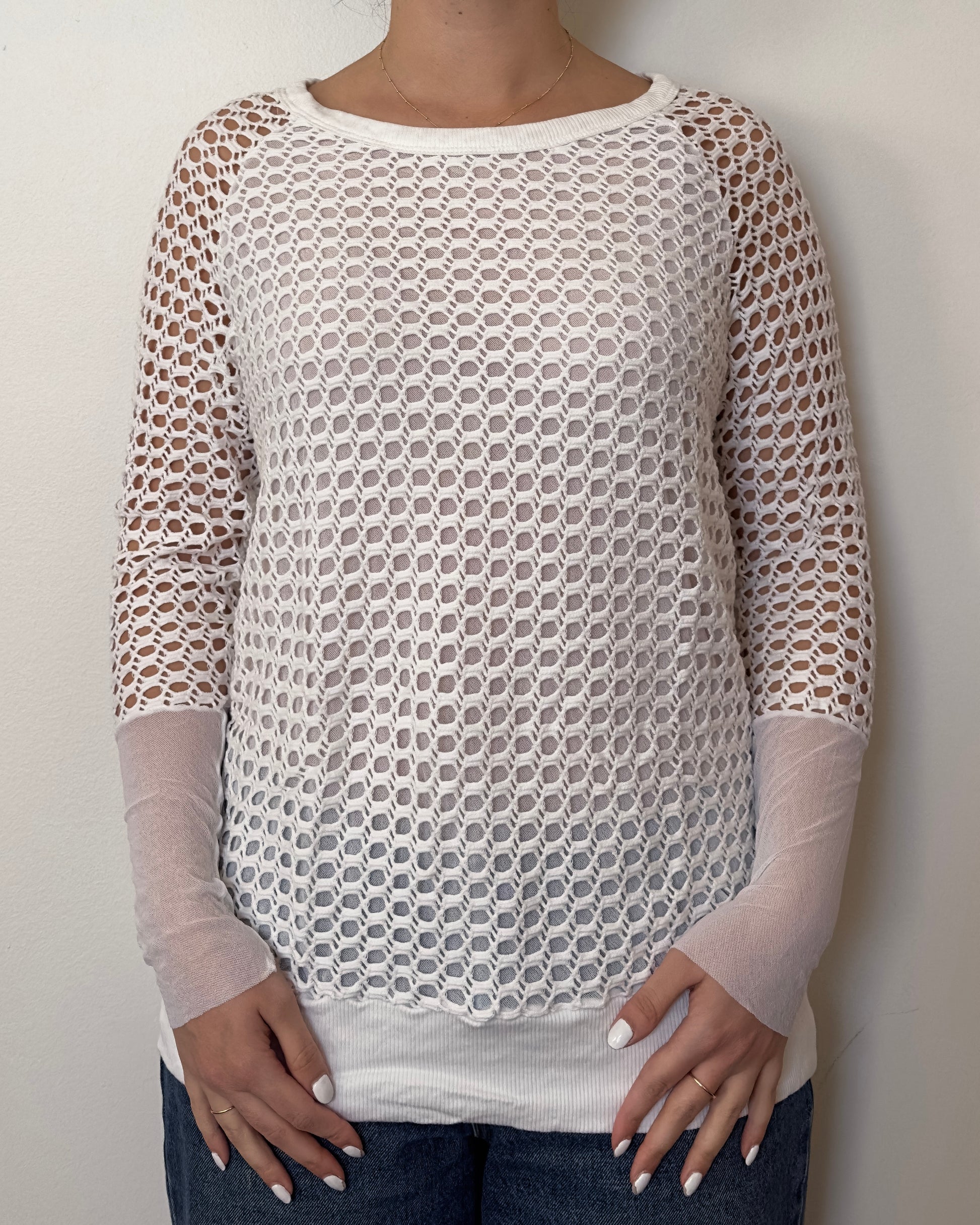 Female model wearing a crochet long sleeve top with part mesh sleeves in a white color with a crew neck cut