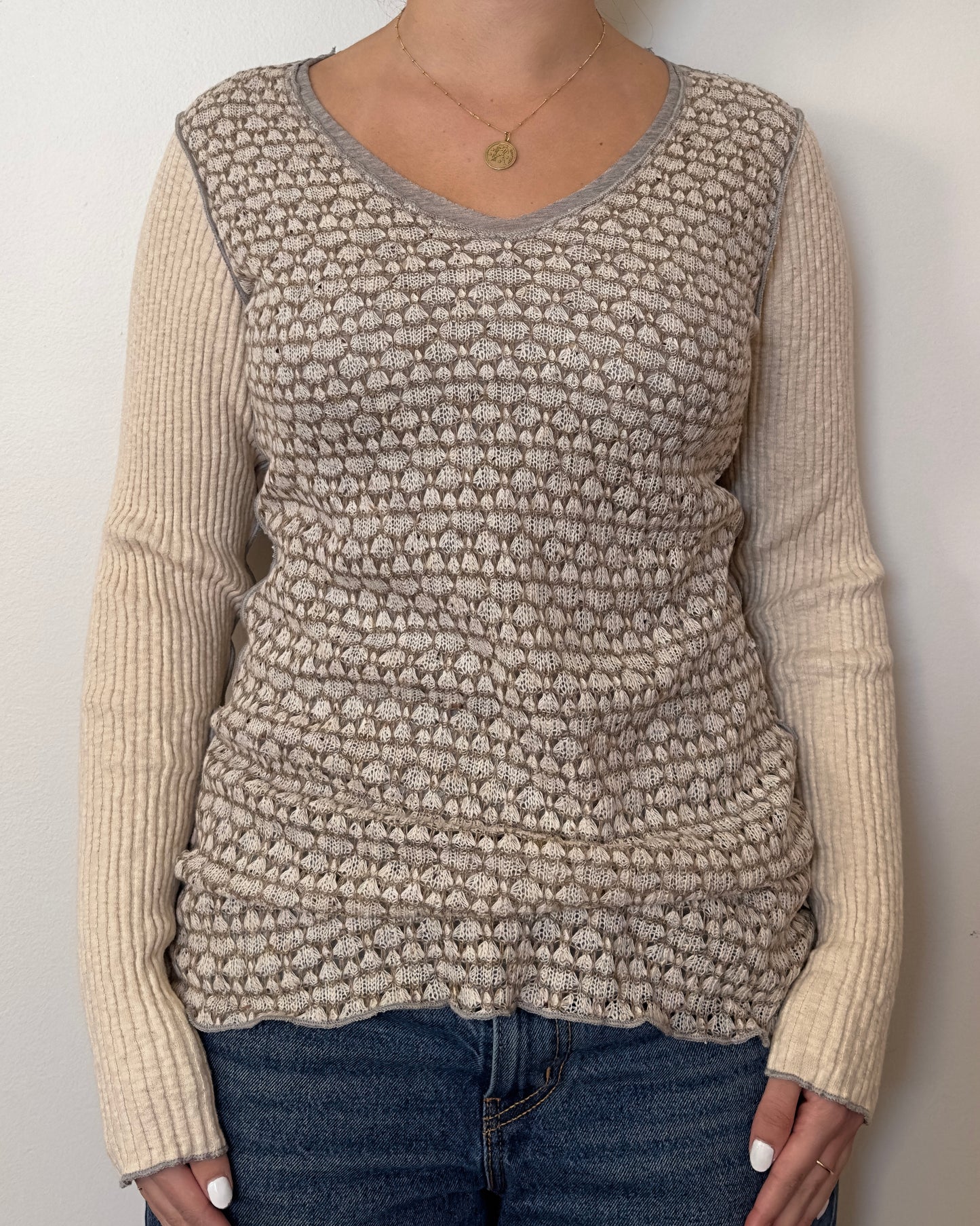 Female model wearing a patterned v neck long sleeve shirt in a beige, brown, and grey color.