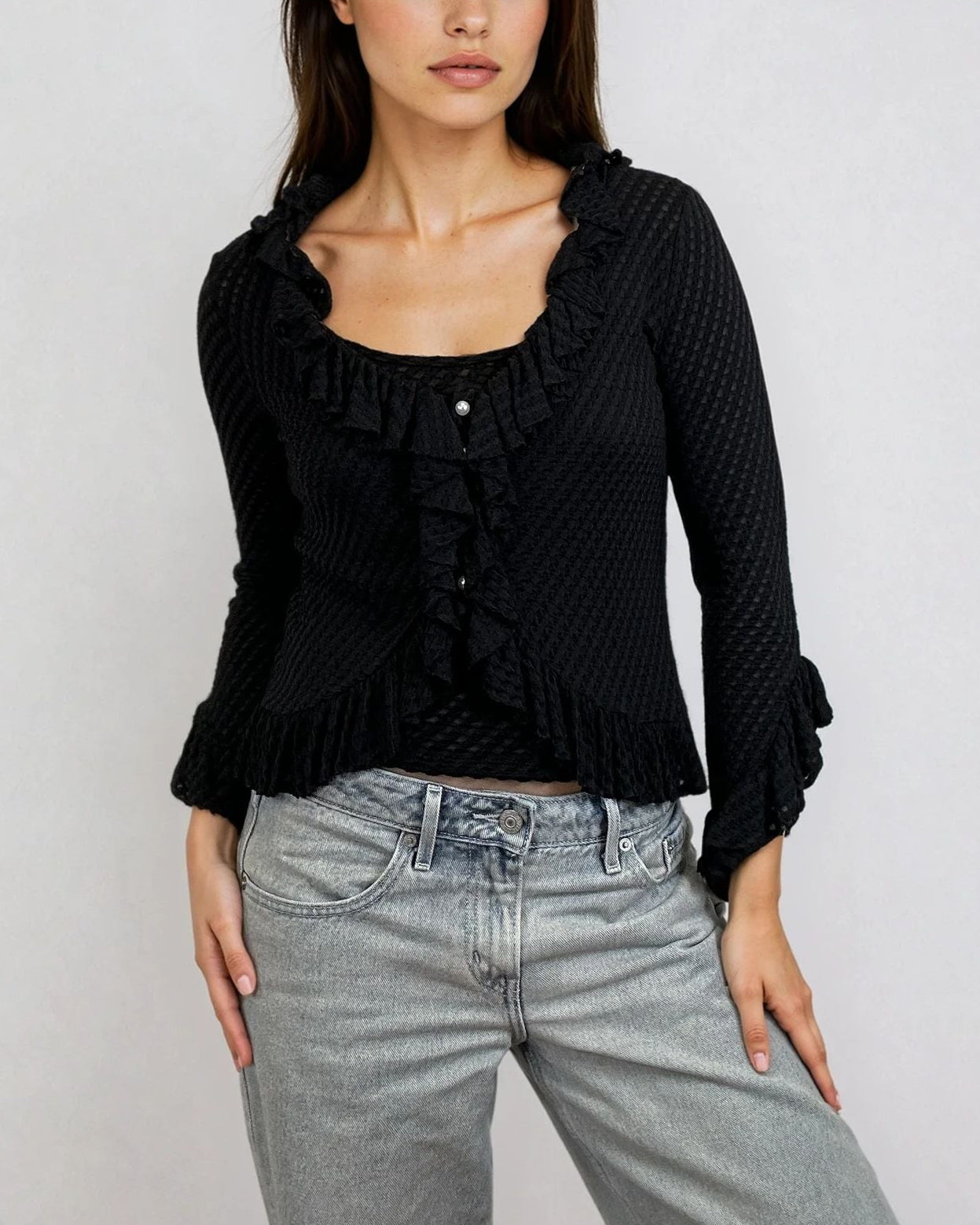 Female model wearing a lightweight jacquard knit with ruffle trim along neckline, hem, and sleeves. Pearl-style front buttons. Flared sleeves. Slightly cropped silhouette. Black. Noir. 