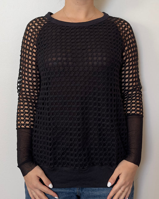 Female model wearing a crochet long sleeve top with part mesh sleeves in a black color with a crew neck cut